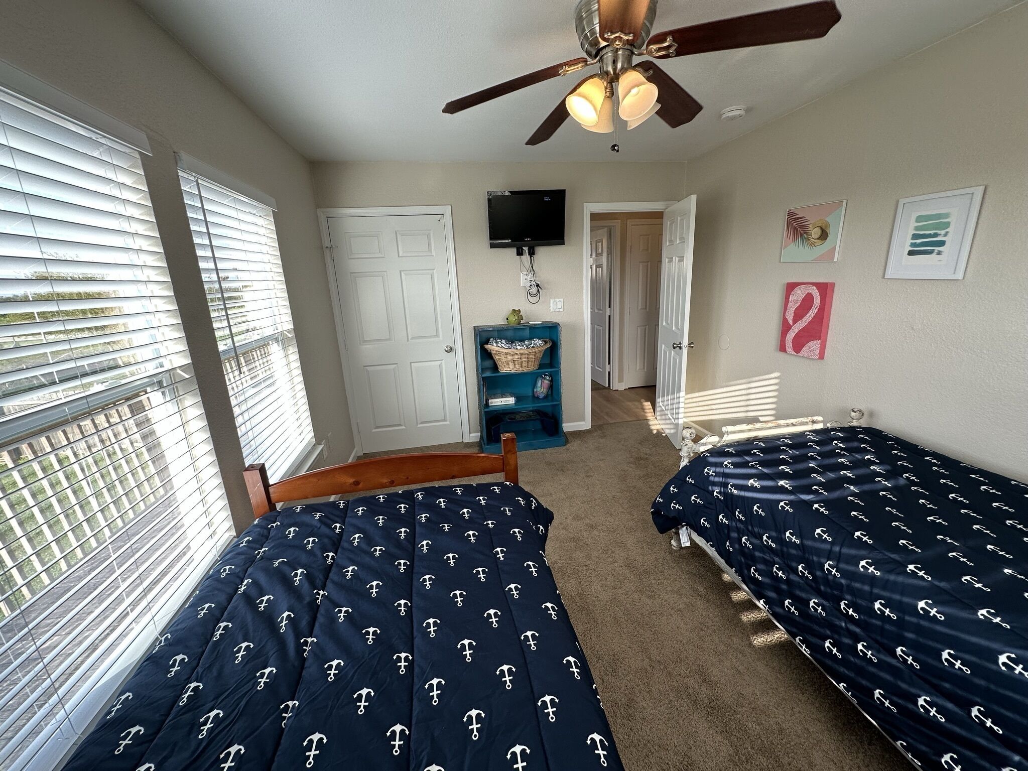 A bedroom with two beds, a ceiling fan, a TV, and a door leading to another room.