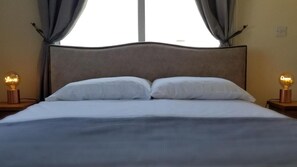 Ein ordentlich bezogenes Bett mit Kopfteil, zwei Nachttischlampen und einem mit Vorhängen versehenen Fenster.