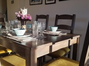 Ein Esstisch, gedeckt mit Kristallgläsern, einer blauen Schüssel und einer Vase mit violetten Blumen.