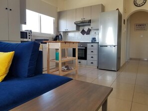 Eine moderne Küche mit Einbauofen, Mikrowelle und Edelstahlkühlschrank. Es gibt einen Holzesstisch und ein blaues Sofa mit einem gelben Kissen.