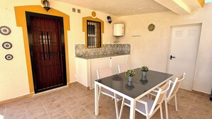 Uma área de refeições com mesa e cadeiras, uma cozinha com painel de azulejos e uma porta com janela.