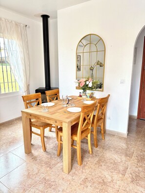 A dining area with a wooden table set for four, surrounded by chairs, a large mirror, and a window with curtains. - Cosy detached villa for 4 persons with private pool, family-friendly (Mazarrón)