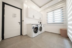 Ein Waschraum mit Waschmaschine und Trockner, weißen Schränken und einem Fenster mit Jalousien.