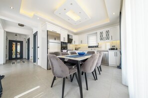 Une cuisine moderne avec des meubles blancs, un réfrigérateur en acier inoxydable et un coin repas comprenant une table et des chaises.