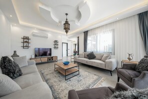 Un salon moderne avec un téléviseur à écran plat, des canapés, une table basse et un tapis à motifs.