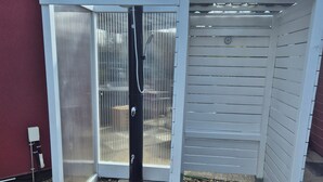 A small, enclosed outdoor shower area with a metal door, a red mat, and a circular drain. - Apartment (Brunsbüttel)