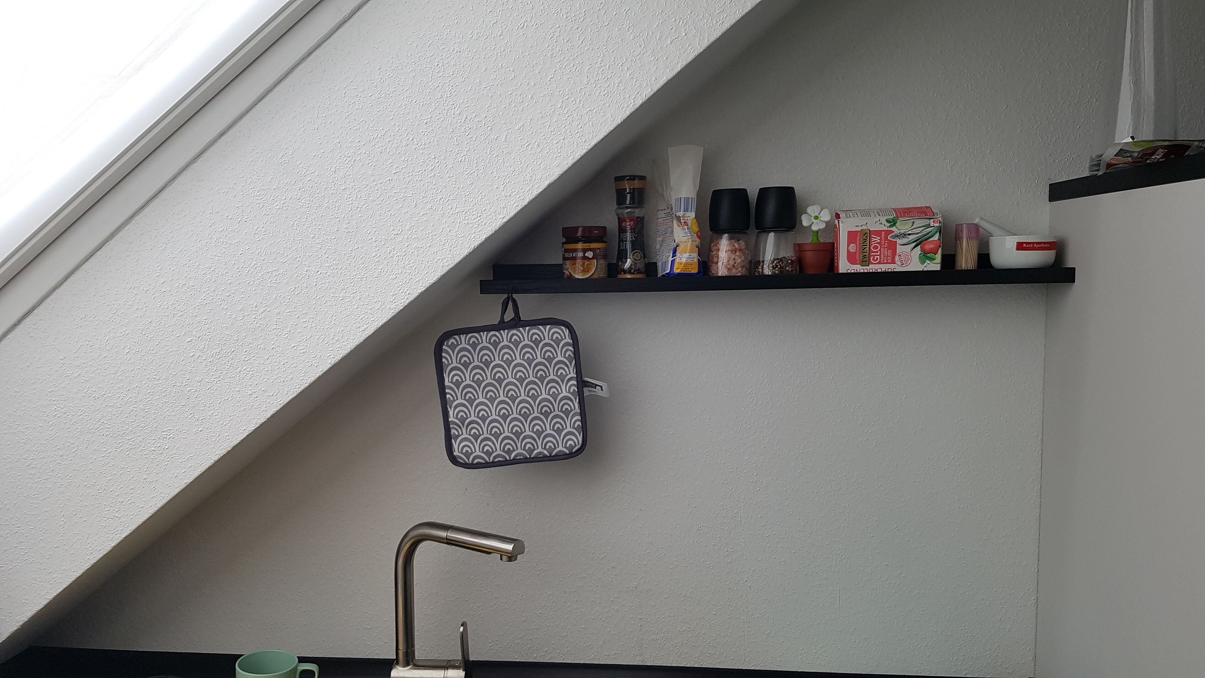 Una cucina con ripiano integrato contenente diversi oggetti, un appendi pentole e un rubinetto.