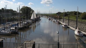 A marina with multiple boats docked along a calm waterway, surrounded by greenery and a clear sky. - Apartment (Brunsbüttel)