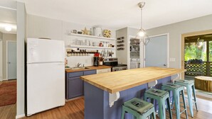 Eine Küche mit einer zentralen Kochinsel, Barhocker, einem Kühlschrank und diversen Küchenutensilien in Regalen.