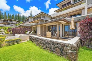 A modern two-story house with a stone retaining wall, outdoor seating, and a view of the surrounding landscape.