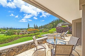 A patio with a glass table and chairs, overlooking a lush garden and a view of a residential area.