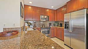 Una cocina moderna con encimeras de granito, electrodomésticos de acero inoxidable, armarios de madera y luces empotradas en el techo.