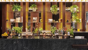 A bar area with a marble countertop, shelves with plants, and various bottles and glasses.