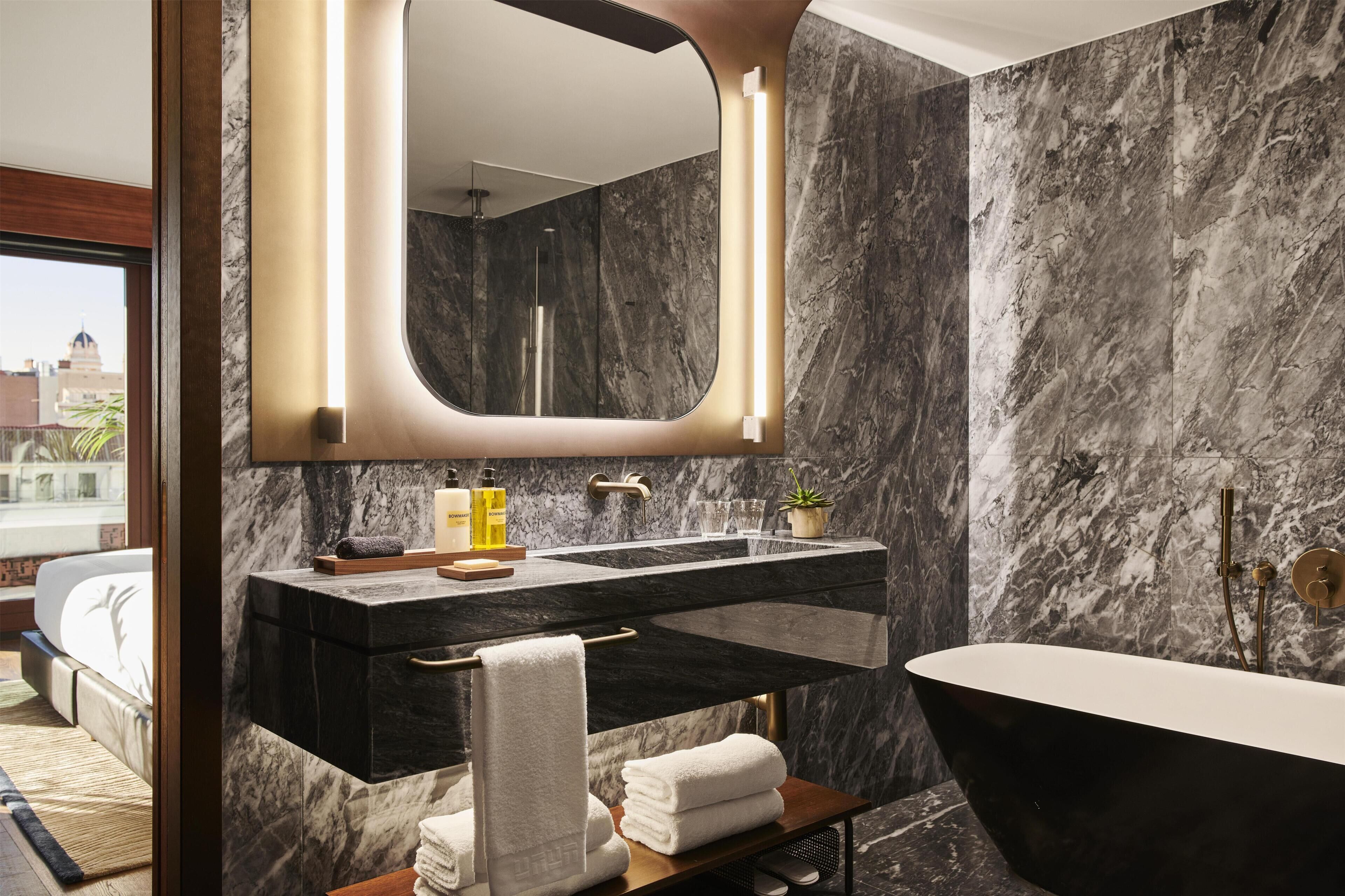 A modern bathroom with a black bathtub, a large mirror, and marble walls.