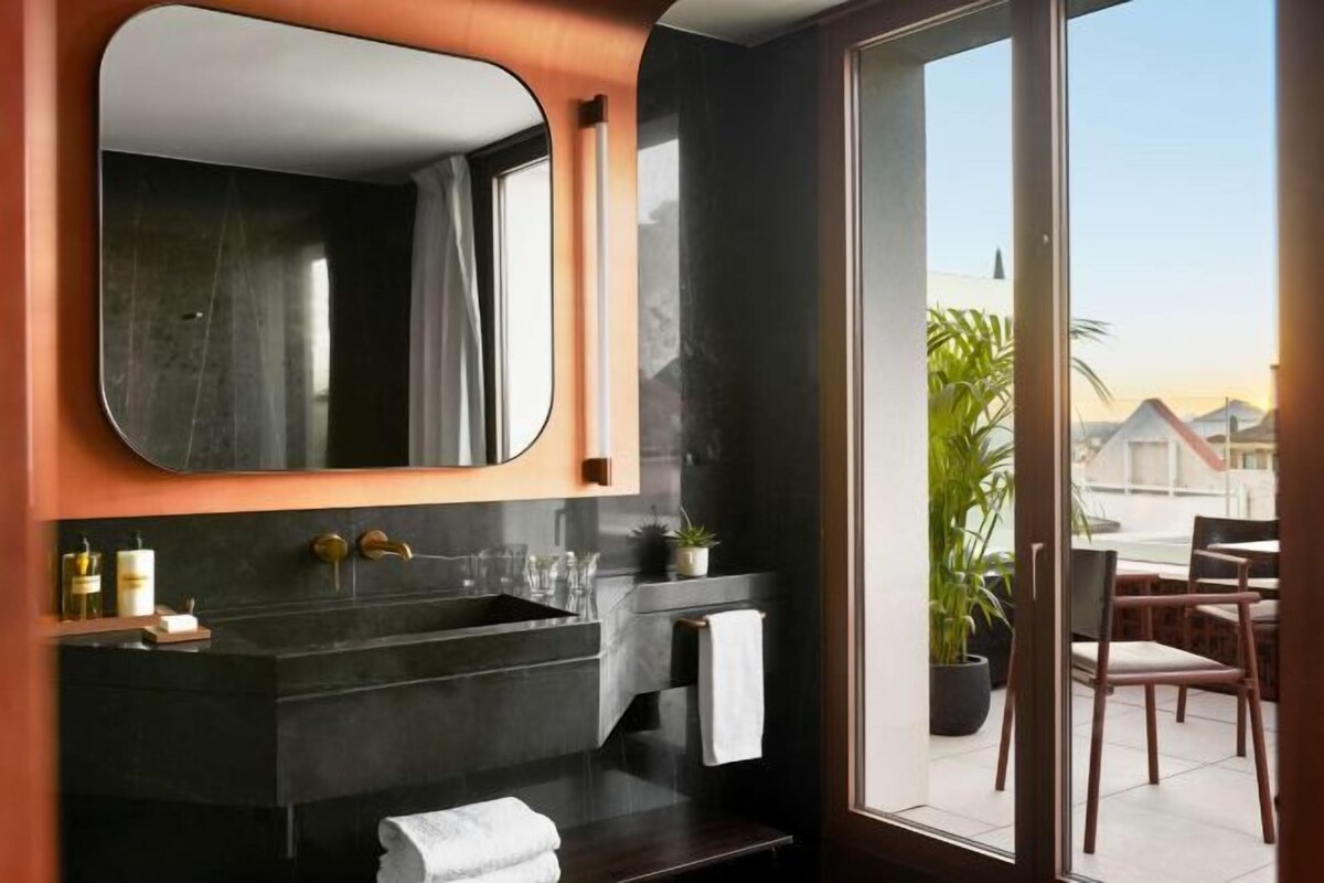 Une salle de bain moderne avec un grand miroir, des plans de travail de couleur sombre et une vue sur l’extérieur.