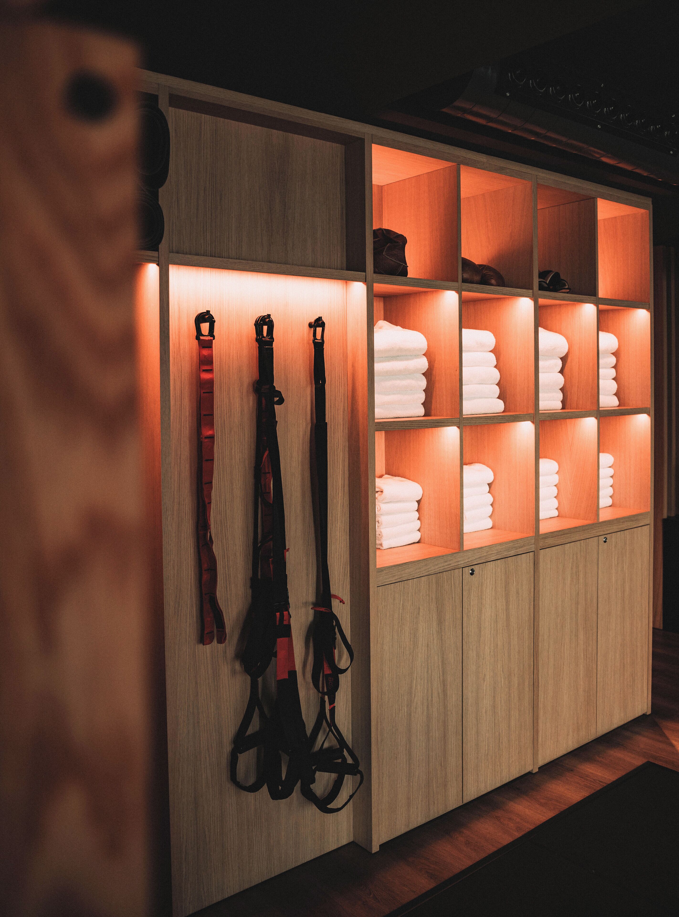 A wooden cabinet with shelves containing neatly folded towels and a pair of black harnesses.