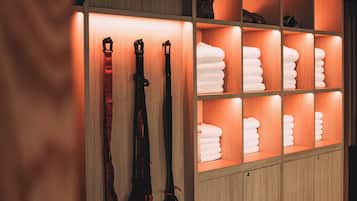 A wooden cabinet with shelves containing neatly folded towels and a pair of black harnesses.