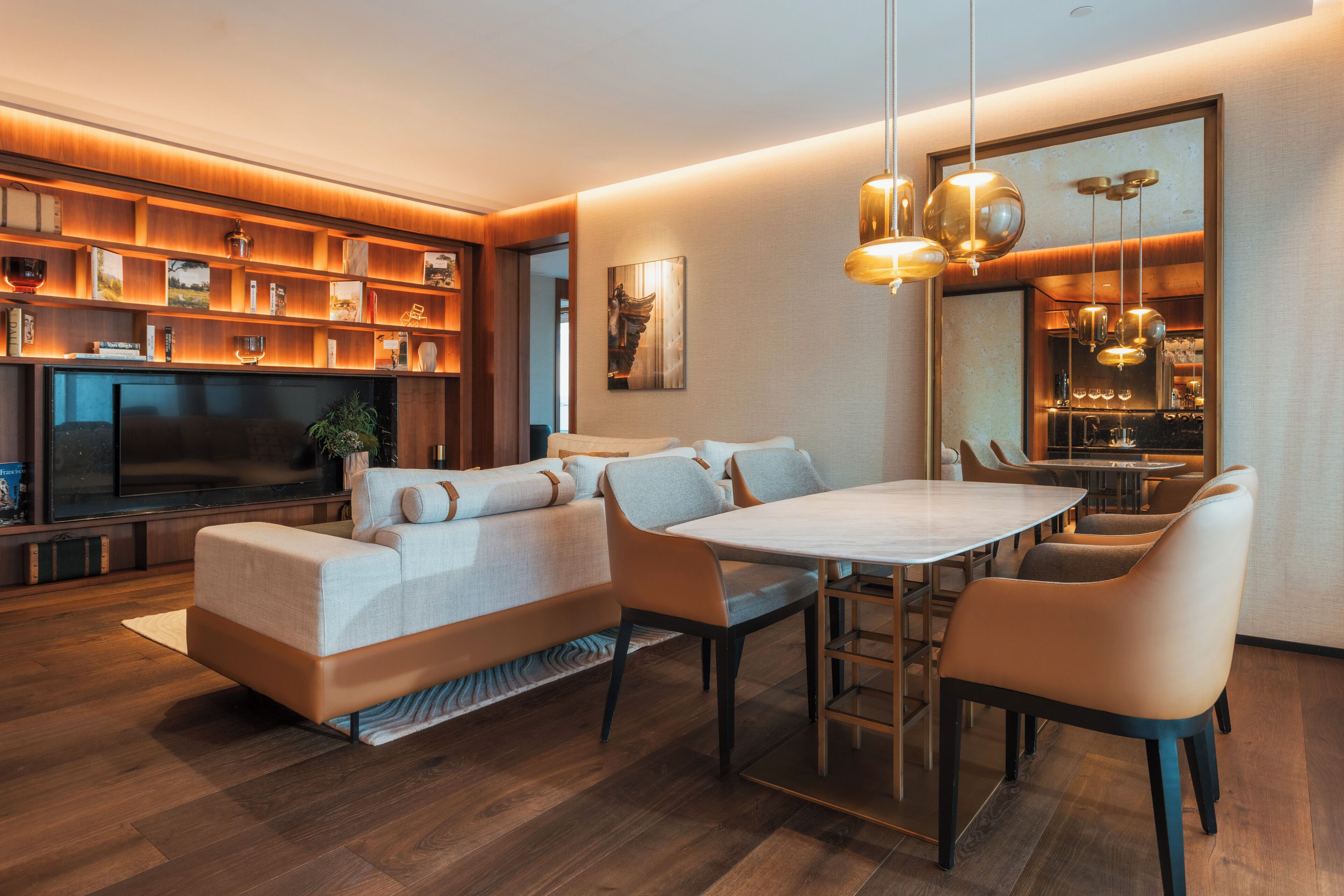 Una sala moderna con un sofá, una mesa de comedor y sillas. Hay un televisor y estanterías con objetos decorativos.