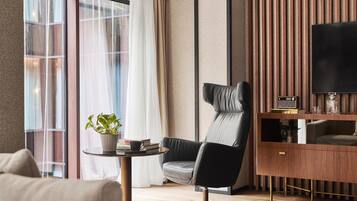 A modern hotel room with a leather chair, a small table with a plant, a flat-screen TV, and a wooden console.