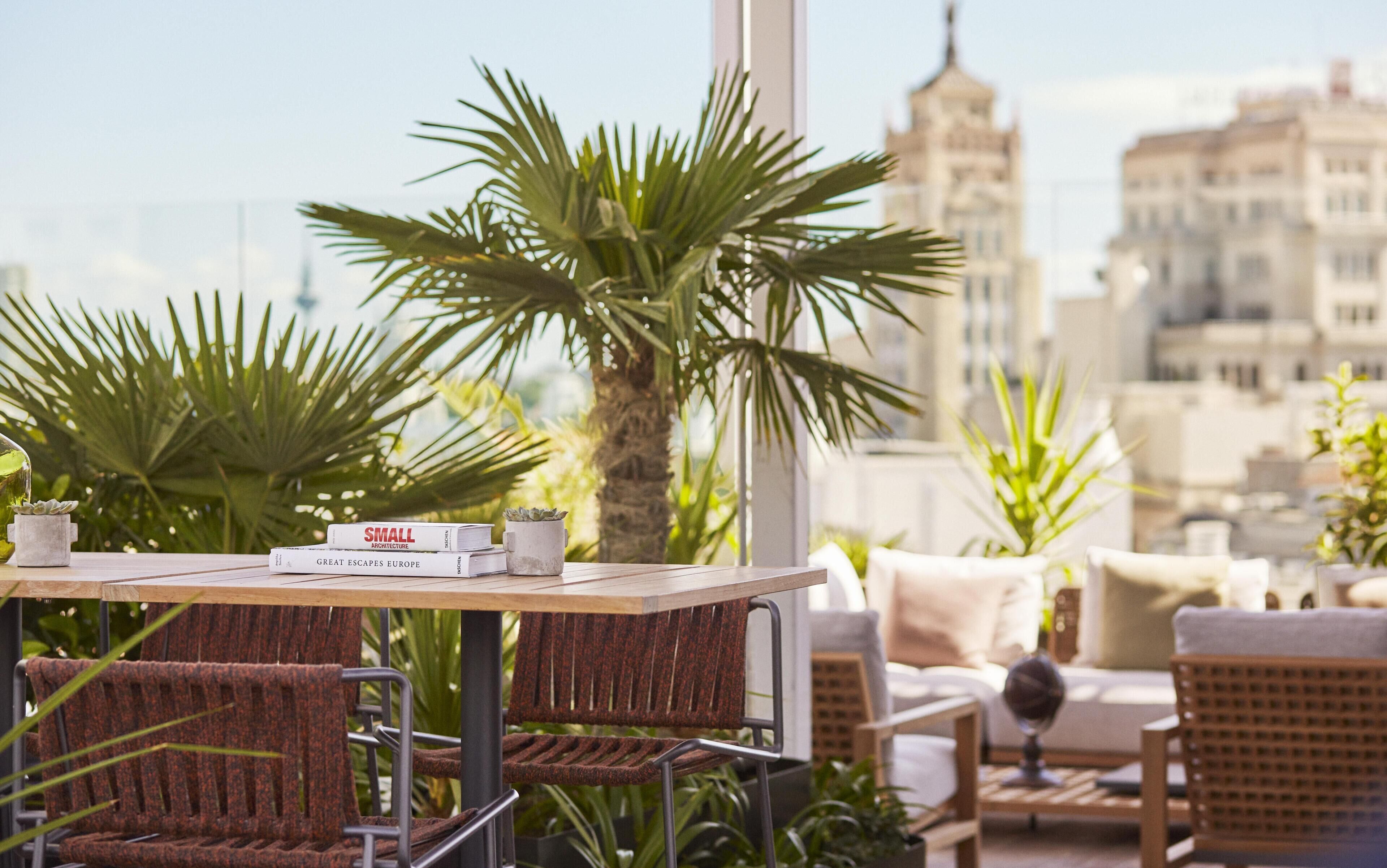 A terrace with wicker furniture, a table with books, and a city view.