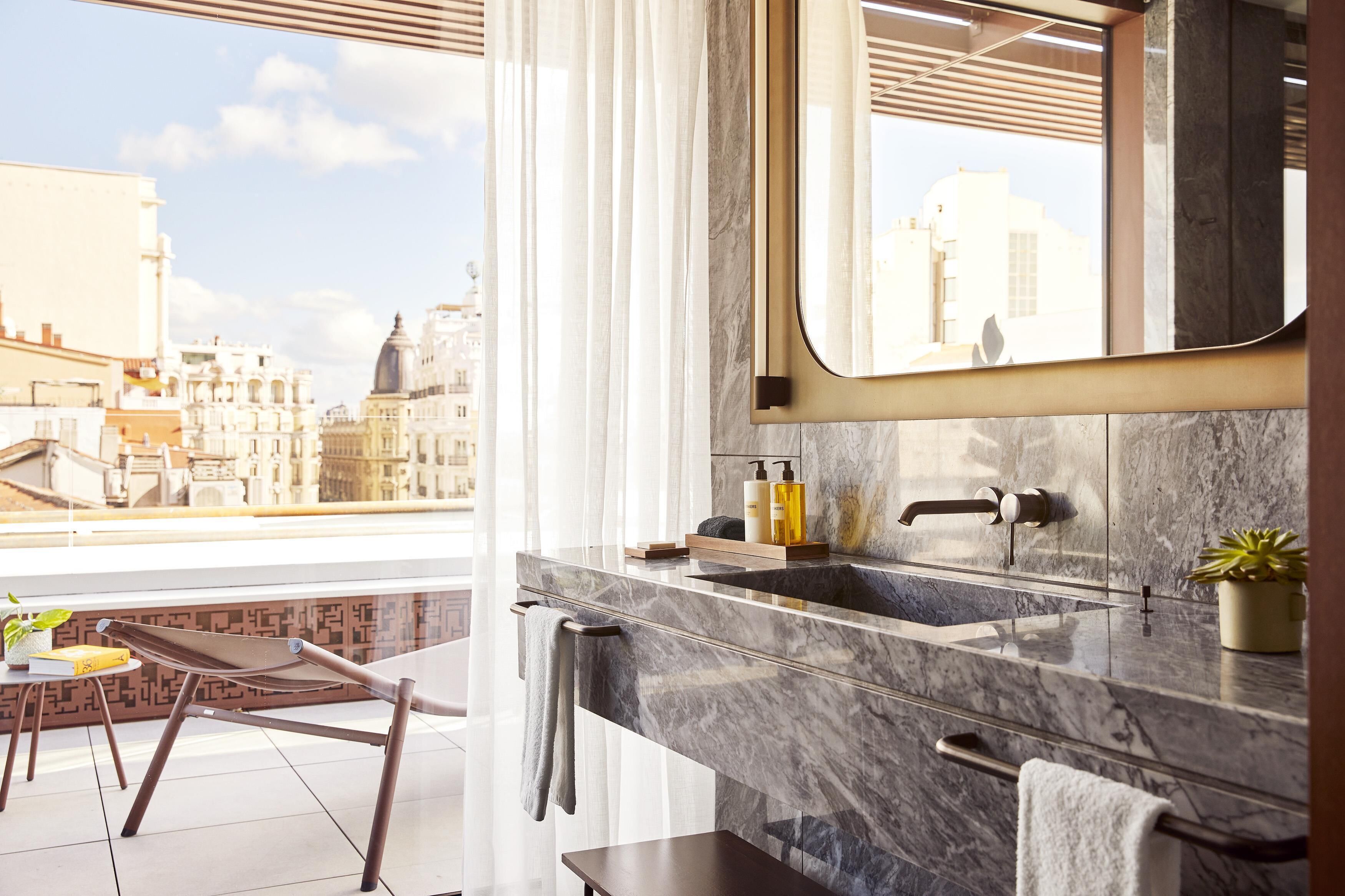 A modern bathroom with a large mirror, marble sink, and a view of the cityscape.