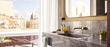 A modern bathroom with a large mirror, marble sink, and a view of the cityscape.