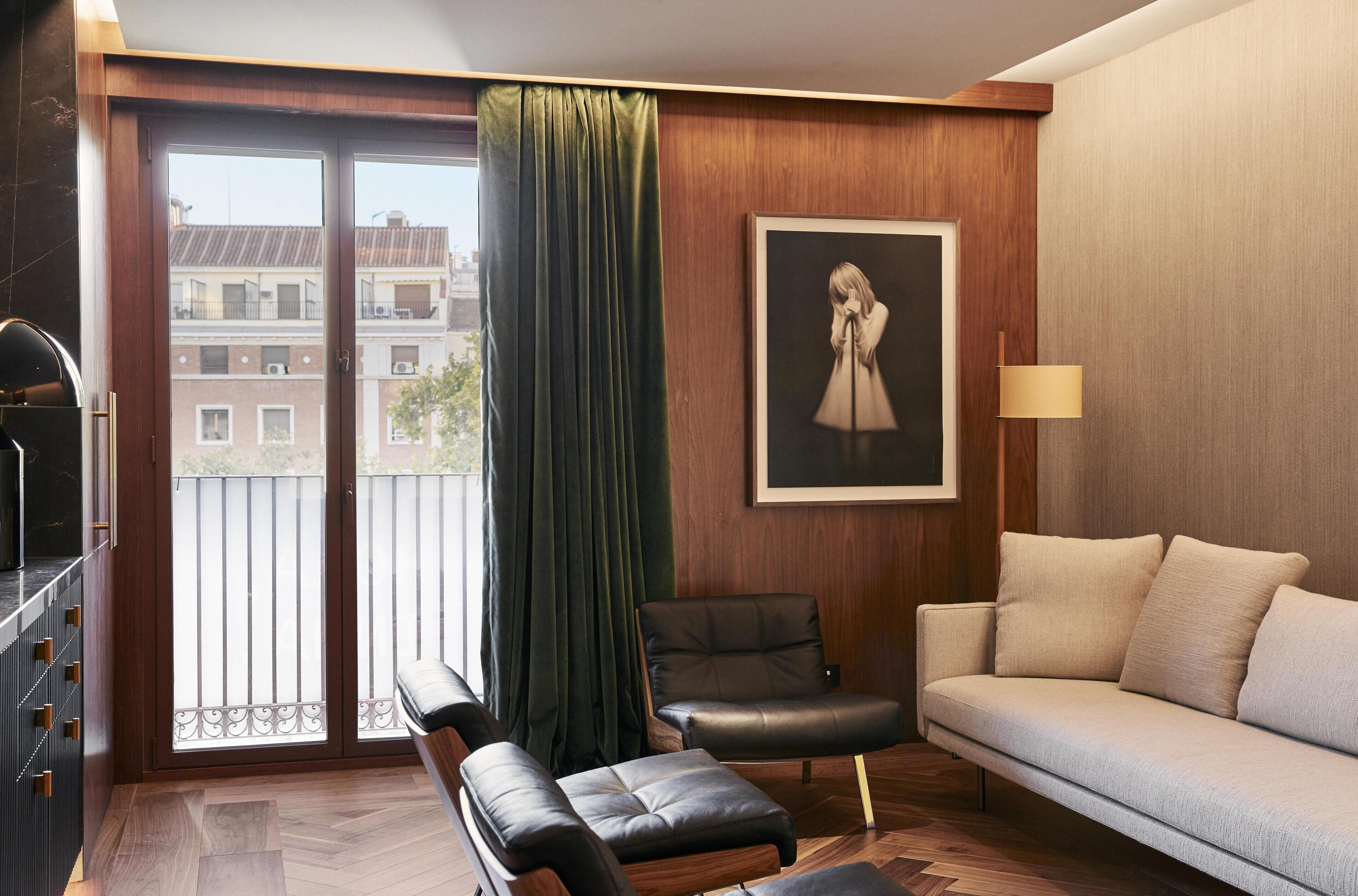Una sala moderna con un sofá, una silla, un banco, un cuadro y vistas a través de una puerta de balcón.