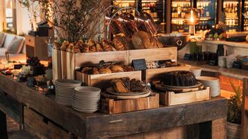 A wooden buffet table with various baked goods and pastries, surrounded by a bar area with shelves of bottles.