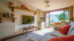 Een gezellige woonkamer met een bank, een televisie, een houten tafel en een keuken die door een open deur zichtbaar is.