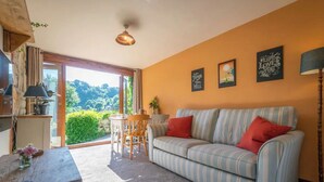 Een gezellige woonkamer met een gestreepte bank, een eettafel met stoelen en uitzicht op groen door een groot raam.