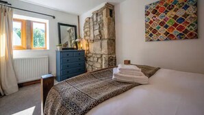 Een slaapkamer met een stenen muur, een bed met een luipaardprintdeken, een dressoir en een kleurrijk kunstwerk aan de muur.