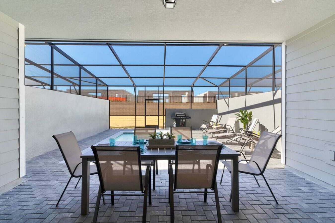 Eine moderne Außenpatio mit einem durch eine Glaswand abgeschirmten Essbereich, einem Pool und Liegestühlen.