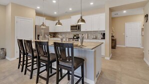 Una cocina moderna con armarios blancos, una isla central con taburetes de bar, iluminación colgante y un microondas.