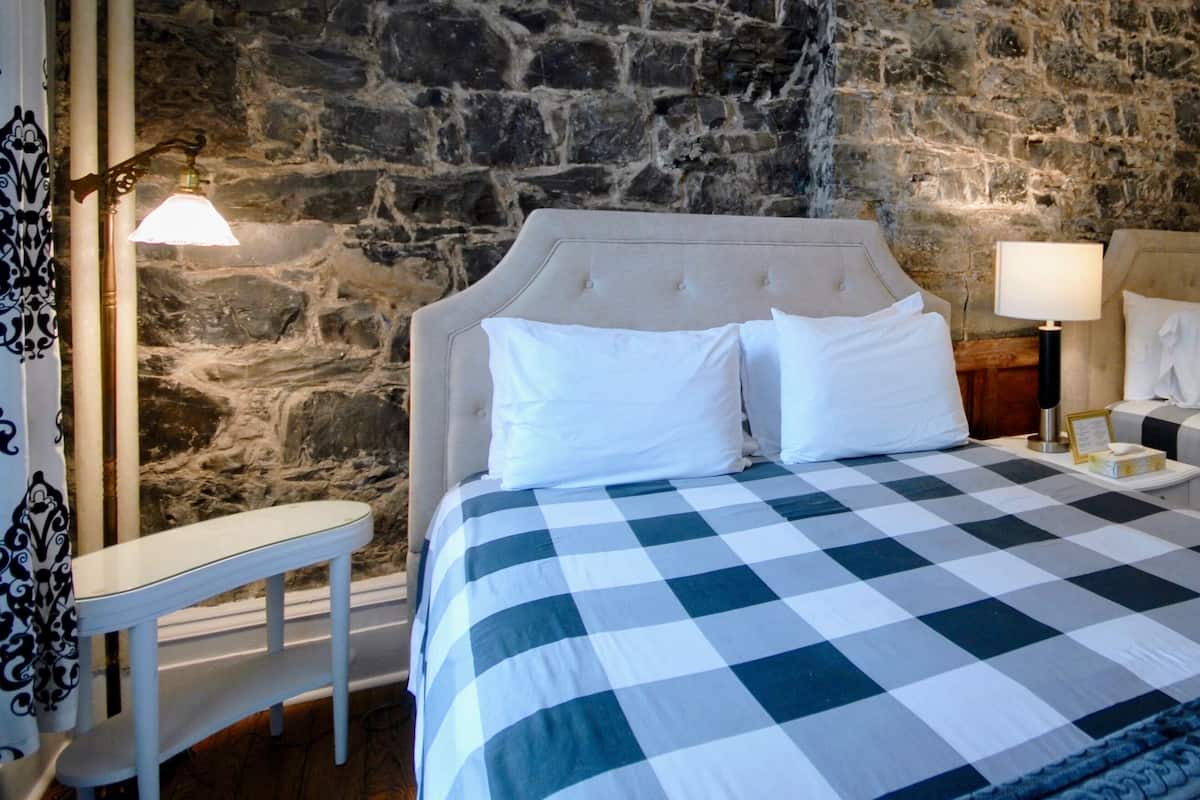 A room with two beds, a stone wall, a small table, and a lamp.