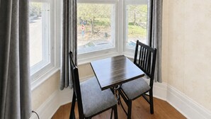 A corner room with a bay window, a table, two chairs, and a view of a tree and building outside. - Manoir Sainte Geneviève (Québec City)