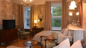 A hotel room with a bed, two armchairs, a small table, a TV, and a desk with a lamp. - Manoir Sainte Geneviève (Québec City)