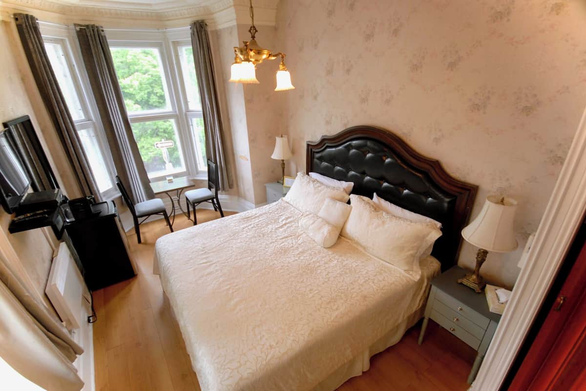 A bedroom with a large bed, a desk, a chair, a television, and a window with curtains.