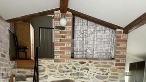 Un coin repas rustique avec une cheminée en pierre, une table et des chaises en bois. Un escalier mène à une mezzanine où se trouvent un meuble en bois et un luminaire suspendu.
