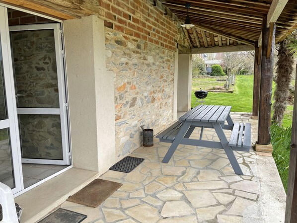 A covered patio with a stone wall, a wooden table, and a grill in the background.