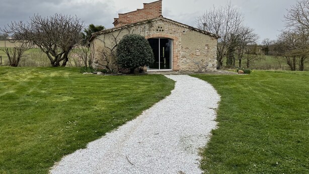 Un bâtiment en pierre avec un chemin de gravier menant à une entrée dotée d’une porte en verre.