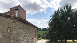 Un bâtiment en pierre avec une cheminée en briques, un chemin en pierre et une zone herbeuse avec des arbres.