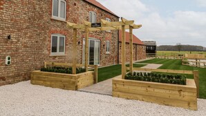 A brick building with a wooden pergola labeled "The Cart House" and raised garden beds with greenery. - The Cart House (York)