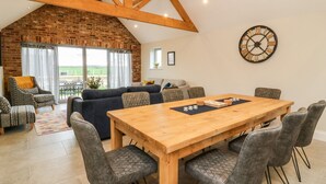 A spacious living area with a wooden dining table, grey upholstered chairs, and a brick wall. - The Cart House (York)