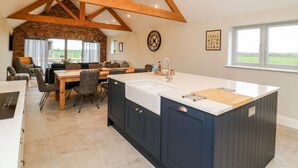 A spacious kitchen with a large island, wooden beams, and a view of the outdoors. - The Cart House (York)