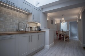 Cocina moderna con armarios blancos, encimera de madera y salpicadero con diseño. Cuenta con un comedor con mesa y sillas, y vistas al exterior a través de una ventana.