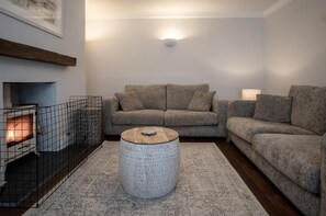 Una sala de estar acogedora con chimenea, un sofá gris, un tapete estampado y una mesa redonda de centro.