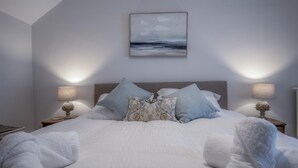 A neatly made bed with white linens, two decorative pillows, and a framed artwork above it. - Noe Acre - 3 Bedroom Cottage - Tenby (Tenby)