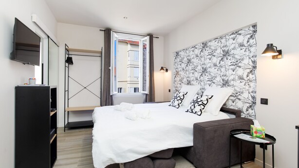 A modern hotel room with a bed, a TV, a desk, and a window with curtains. - Apartment in Cannes (Cannes)