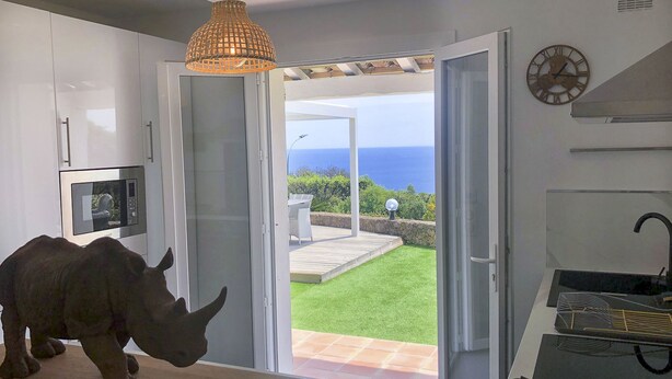 A kitchen with a view of the ocean, a dining area with a table and chairs, and a large window. - Bleu Comme Toit 3425 (Les Issambres)