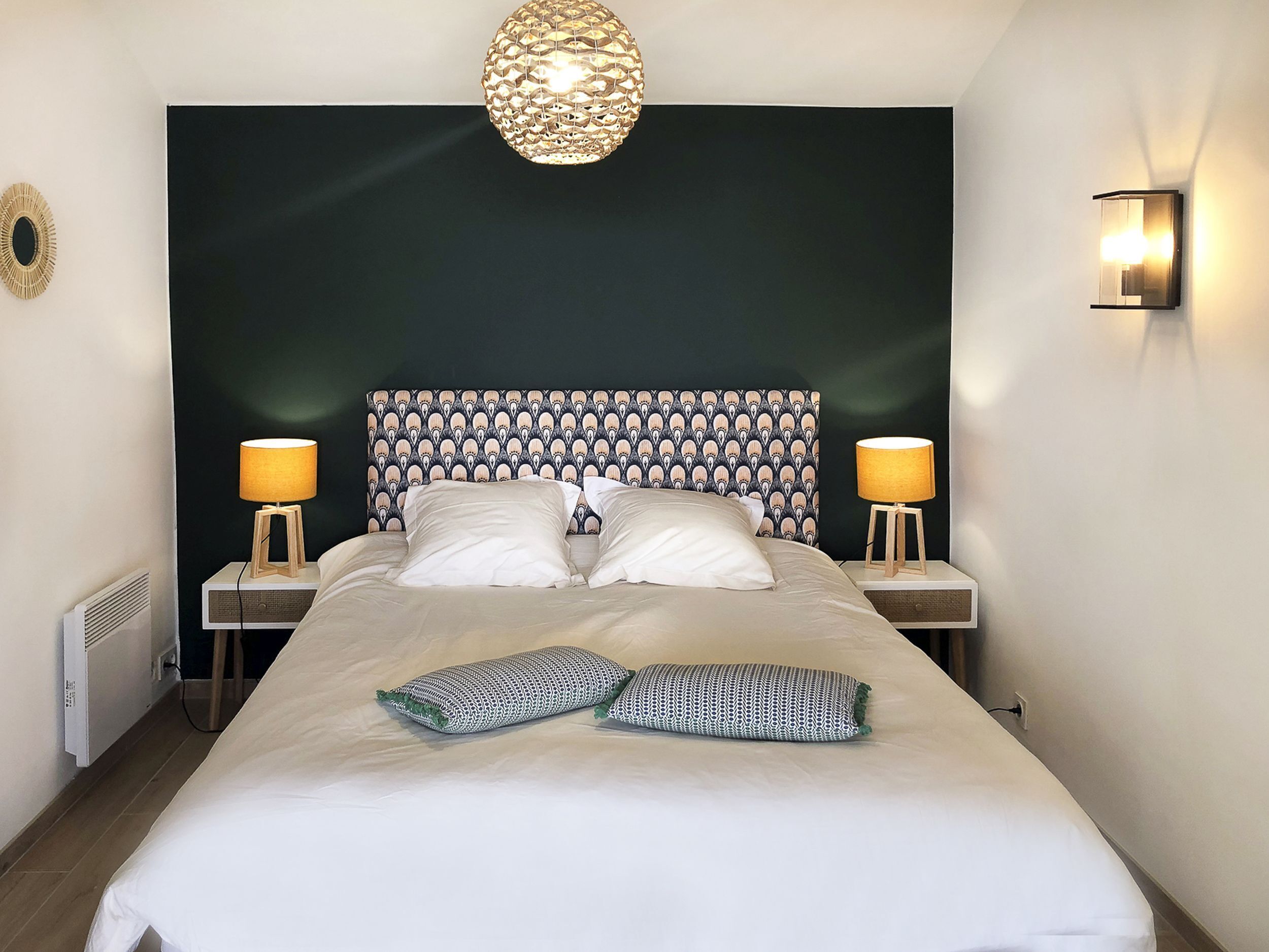 Een netjes opgemaakt bed met twee kussens, een bedlampje en een wandlamp.